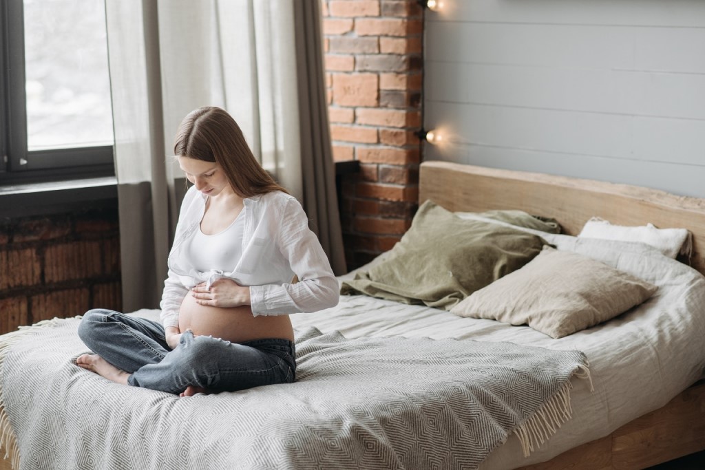 kobieta w ciąży siedzi na łóżku i patrzy na swój ciążowy brzuszek
