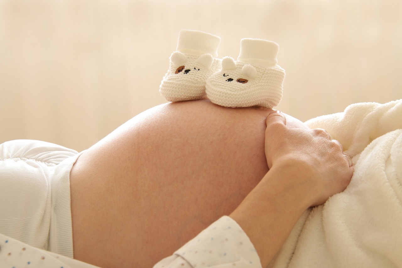 małe buciki zrobione na drutach leżą na brzuchu kobiety w ciąży